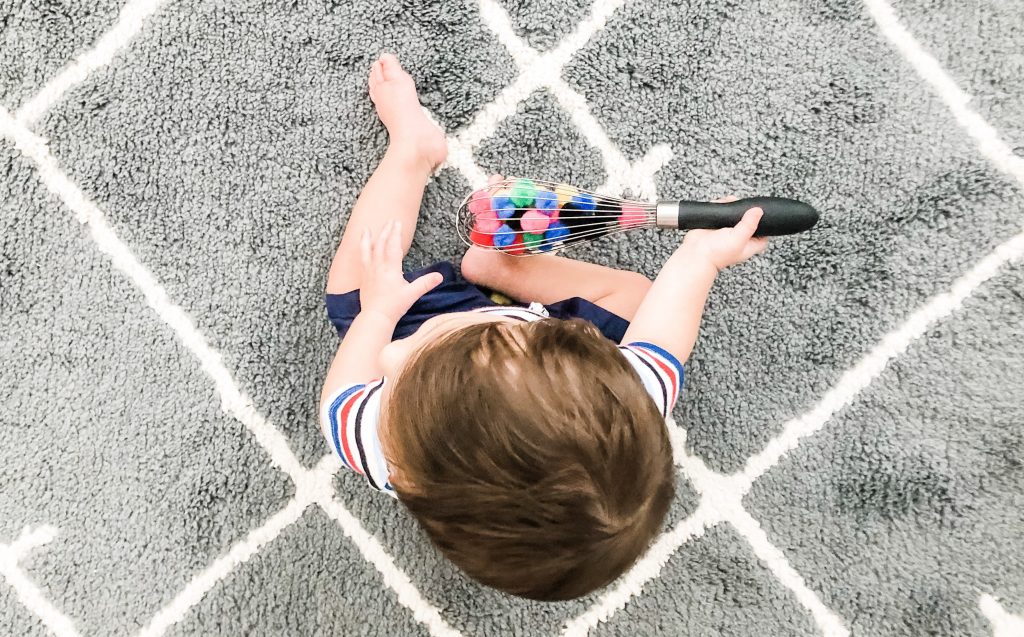 This pompom whisk baby activity works on fine motor skills and learning. Using colored poms is a great fine motor activity for infants 9 months or older.